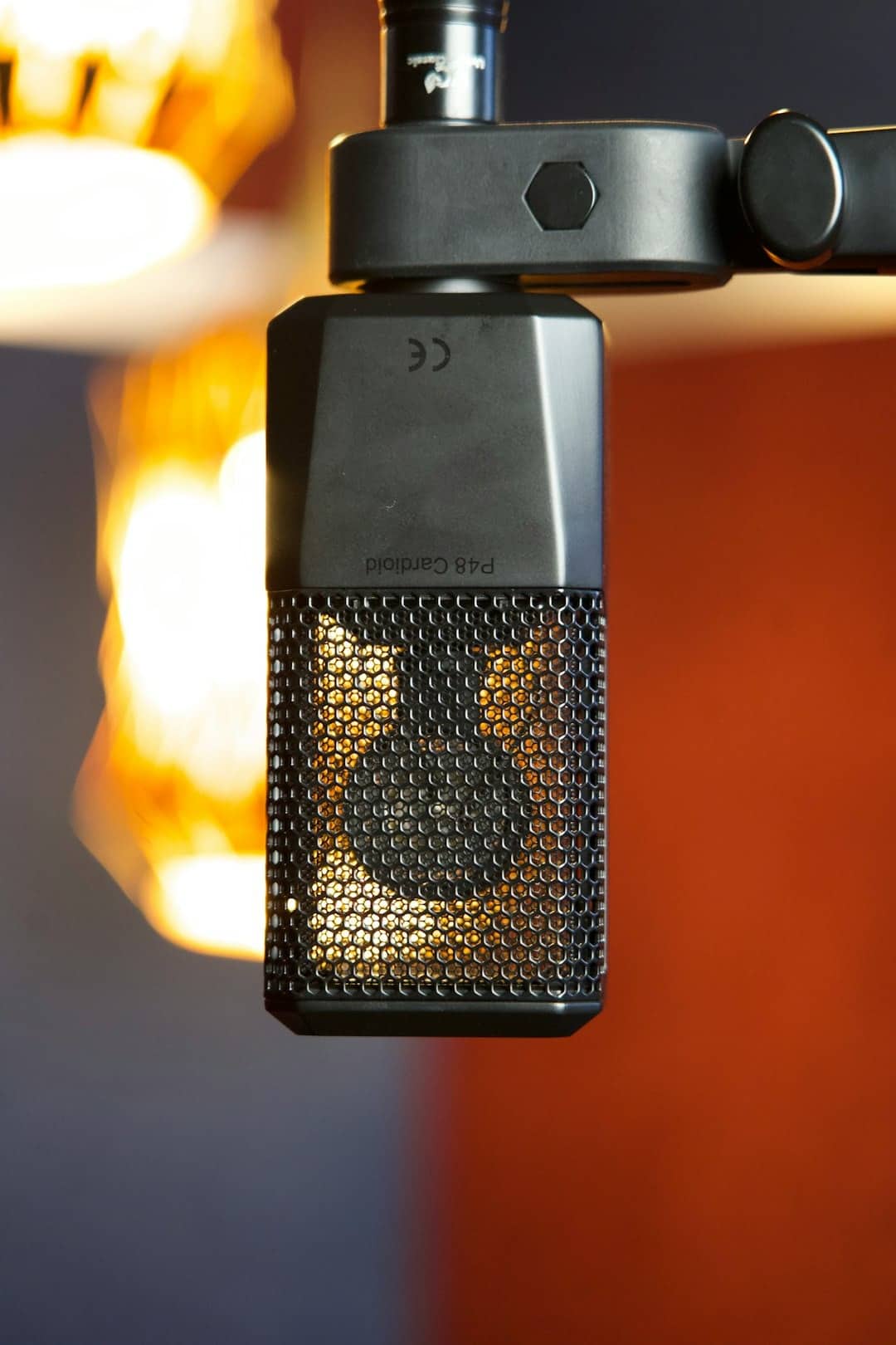 A professional microphone with glowing internal components hanging from a stand.